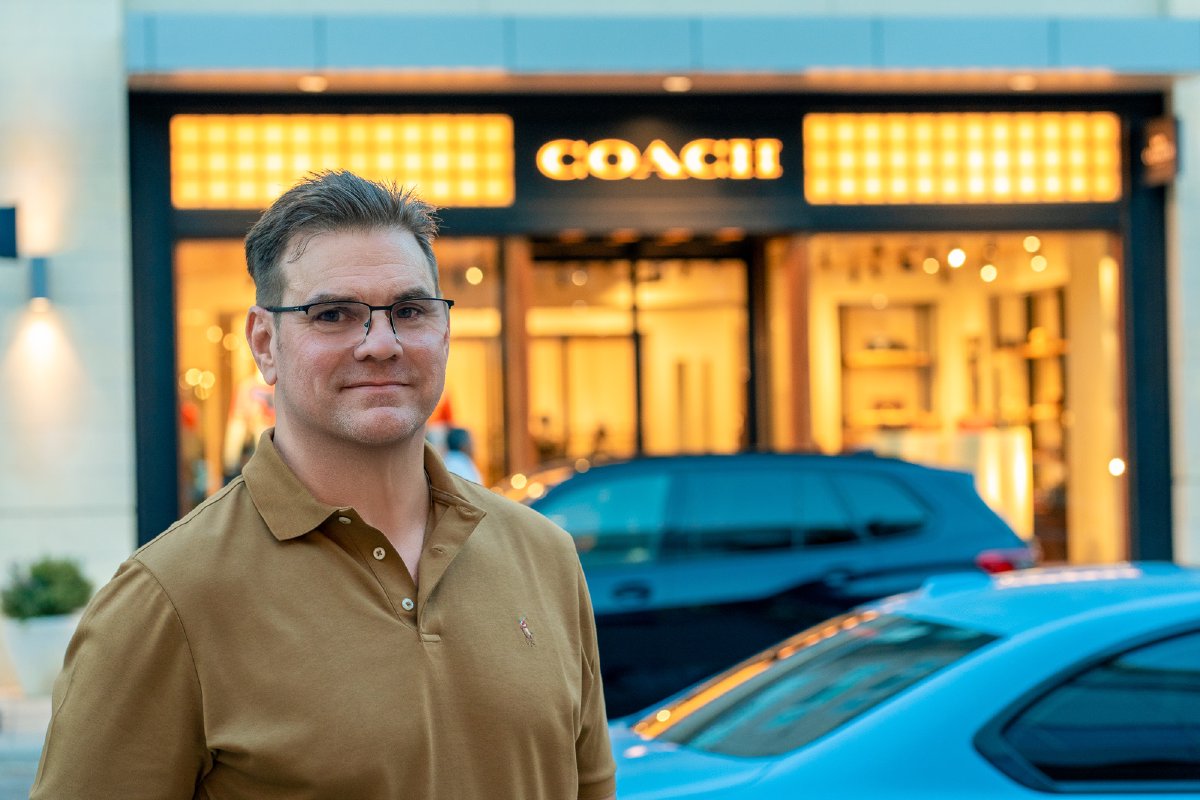 Evening portrait in a tan polo in front of a glowing storefront at Legacy West in Plano