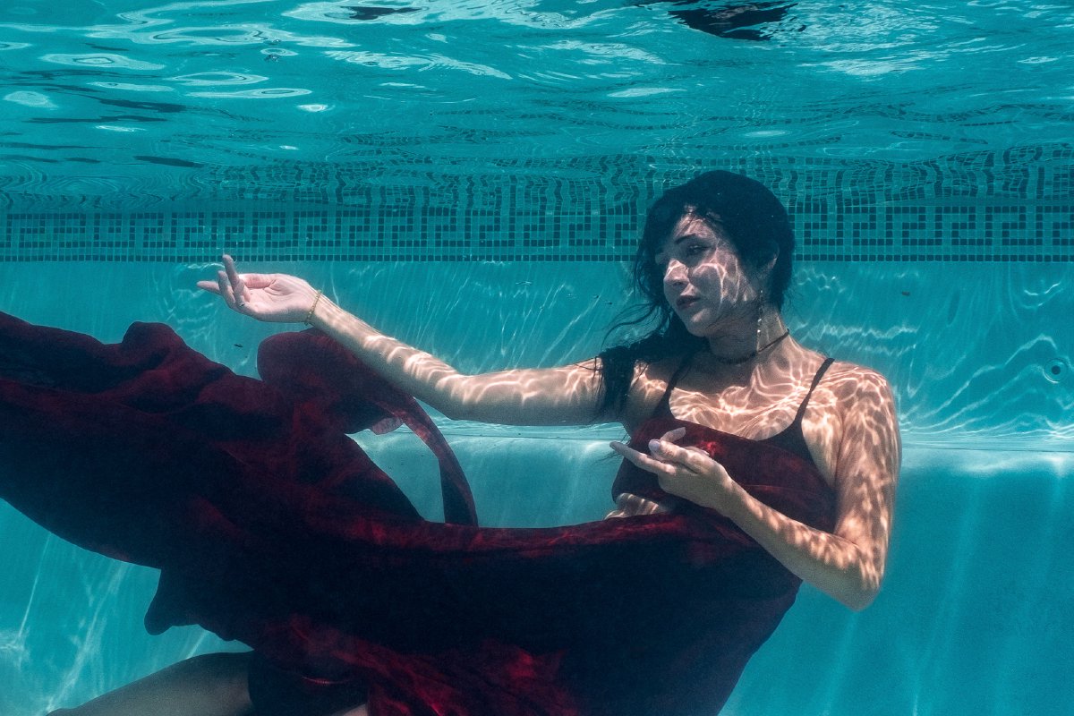 Underwater portrait with deep red fabric drifting through turquoise pool water