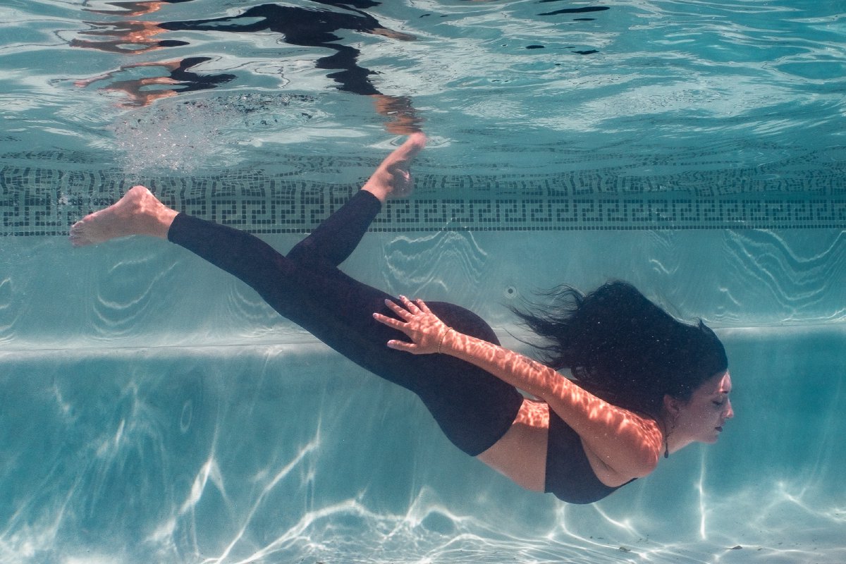 Underwater portrait near the surface with sunlight patterns across the model's face and arm