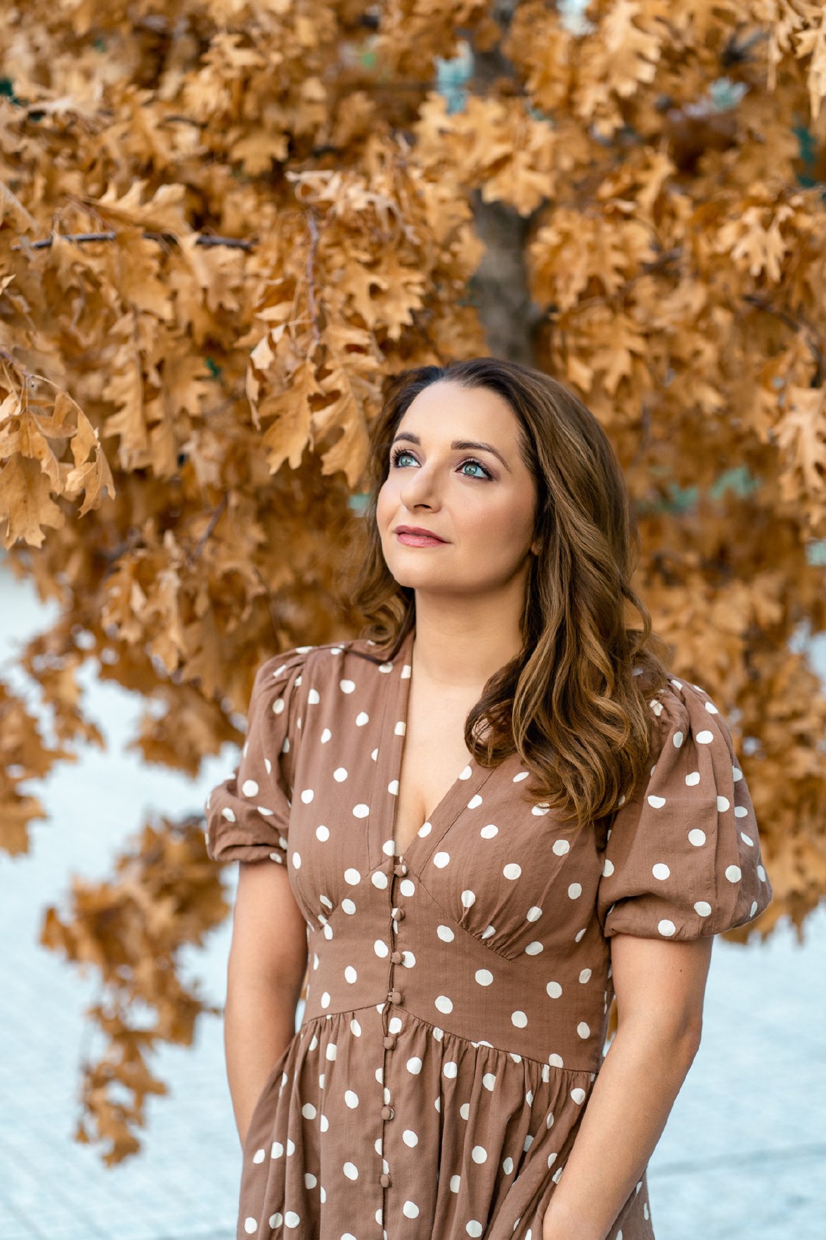 Soraya Mafi in a polka dot dress looking up, framed by orange oak leaves