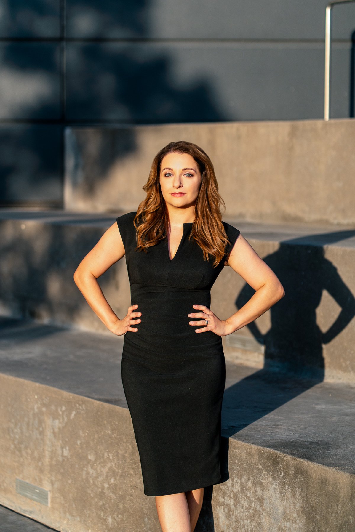 Soraya Mafi in a fitted black dress with hands on hips on concrete steps, low morning sun and long shadows
