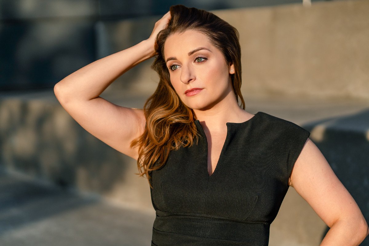 Close-up in a black dress in warm morning sun, one hand pushing back her hair