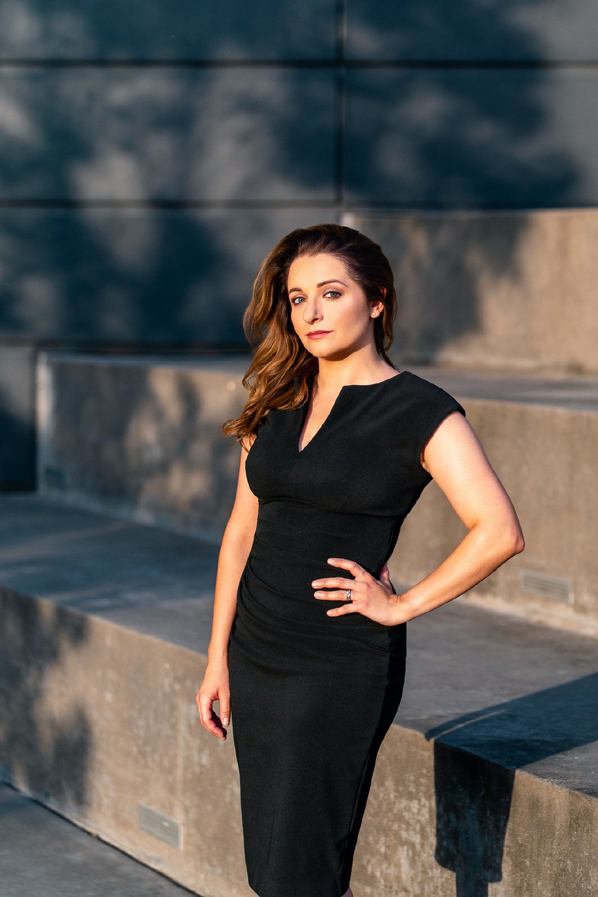 Black dress portrait in warm morning light, hand on hip, looking straight at the camera