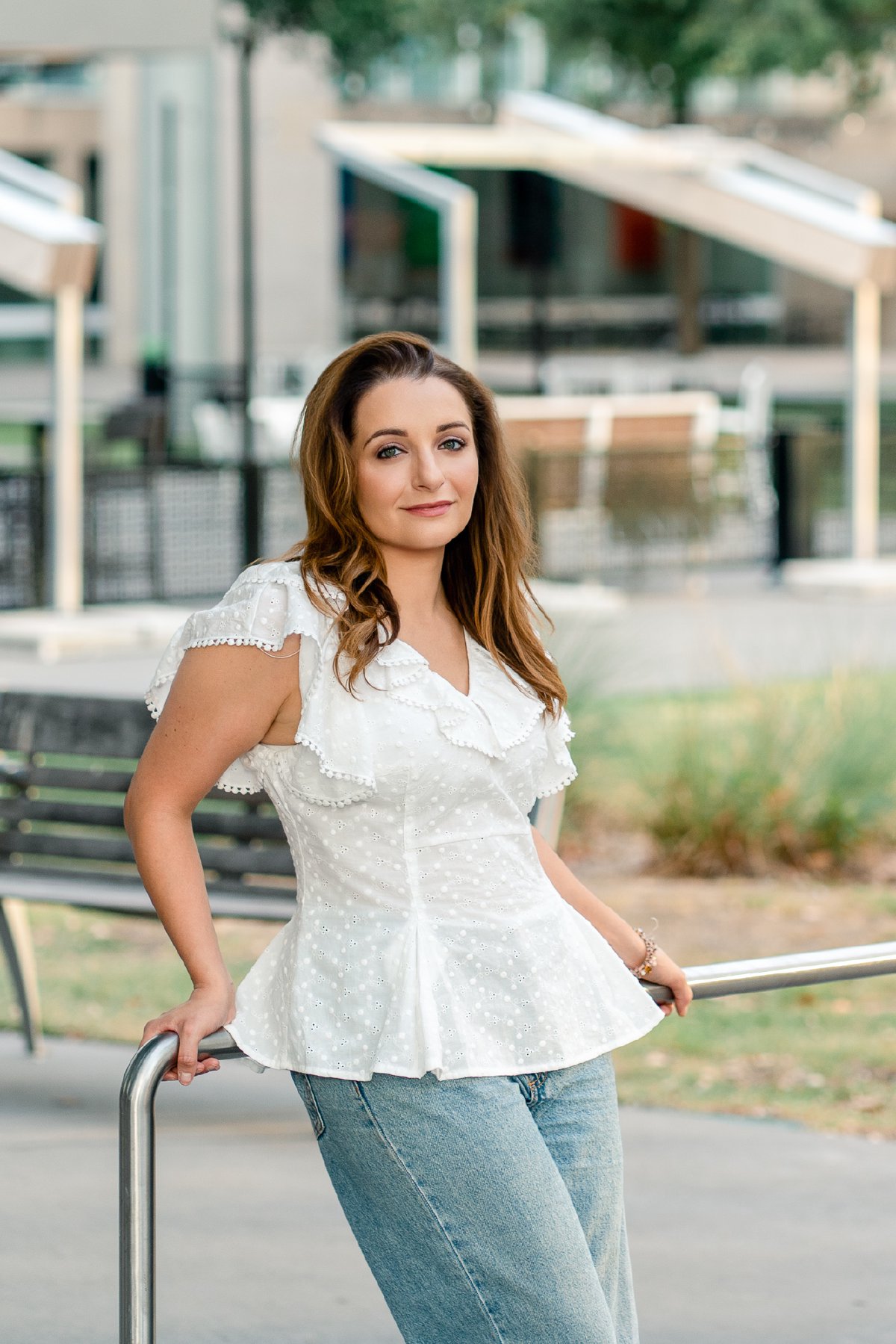White ruffled top and wide-leg jeans, leaning on a railing with a soft smile