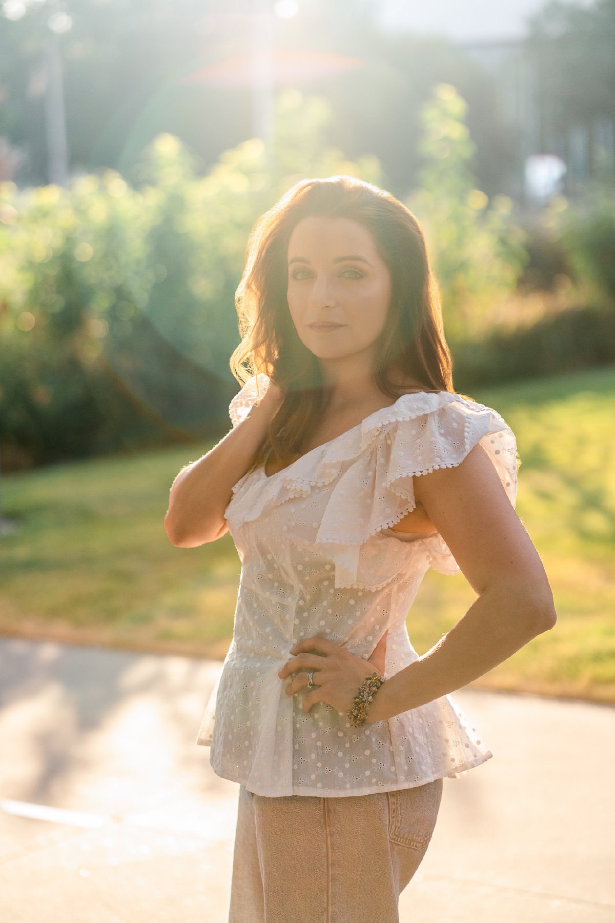 Backlit portrait with sun flare, white eyelet top glowing, hand on hip