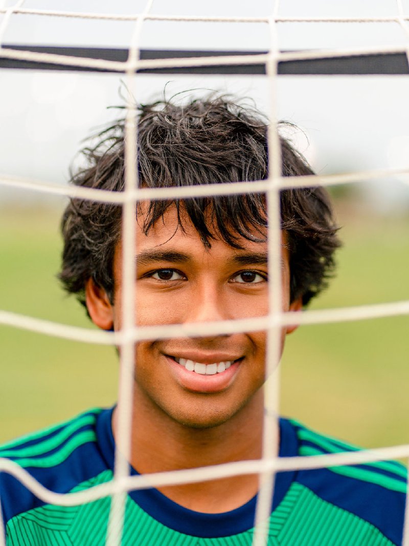 Senior portrait of Brandon behind the soccer net at golden hour in Prosper
