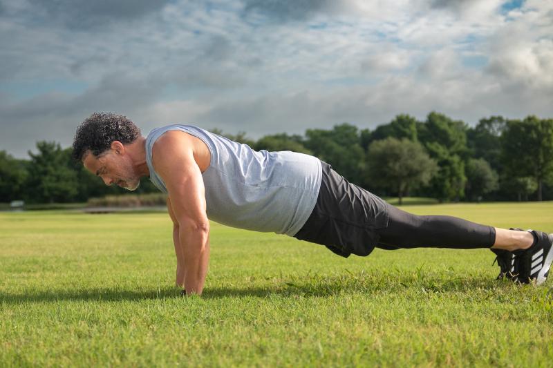 Athletic portrait of Corey holding a push-up position in an open field in Frisco