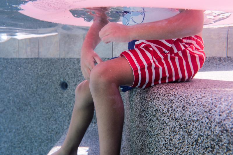 Child sitting on the pool steps seen from underwater with a float overhead during a family pool day