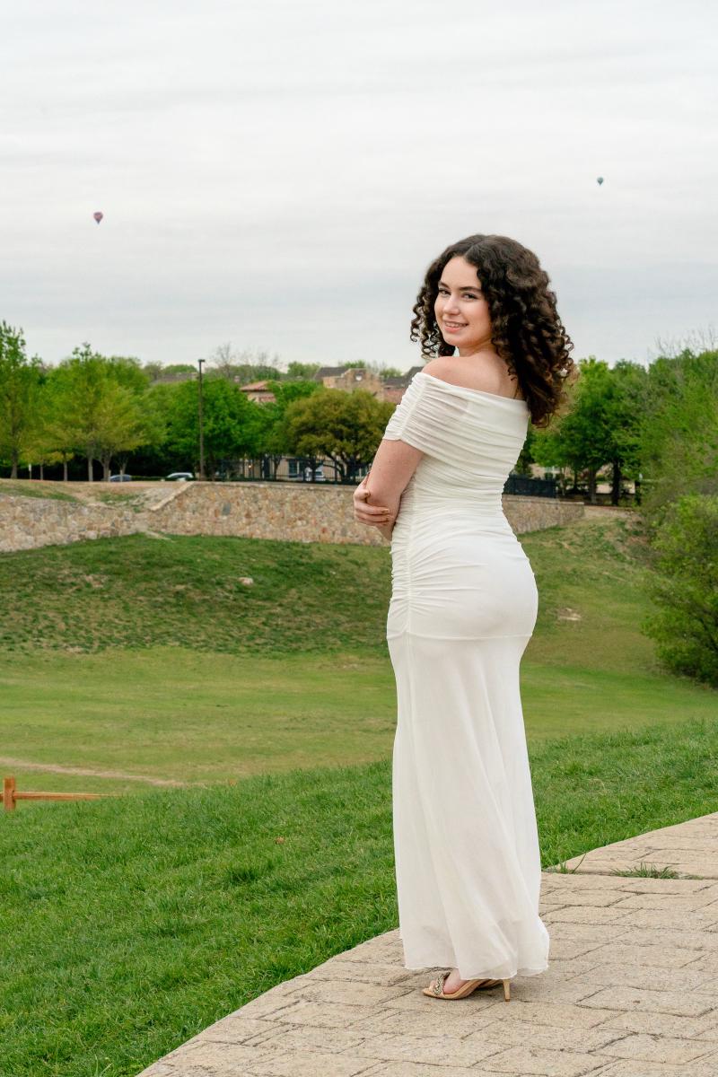 Senior portrait of Sophia in a flowy white dress in an open field with hot air balloons in the Texas sky