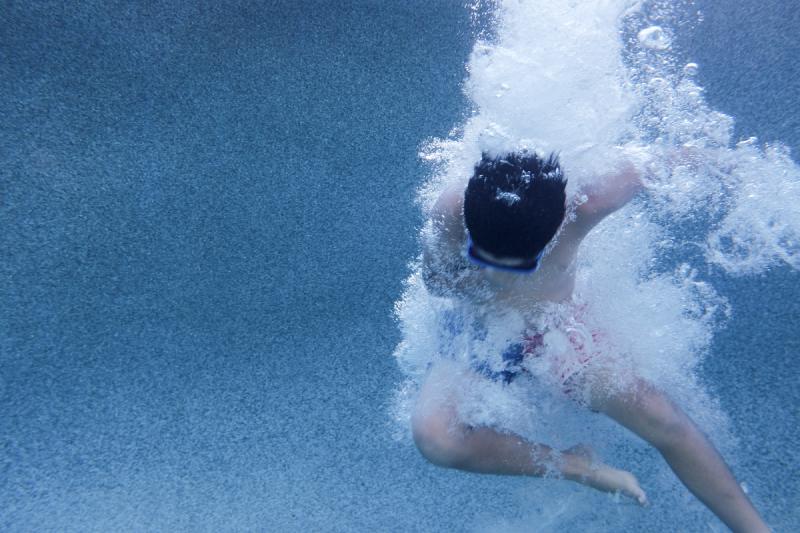 Kid fully underwater in a backyard pool, surrounded by bubbles after going under